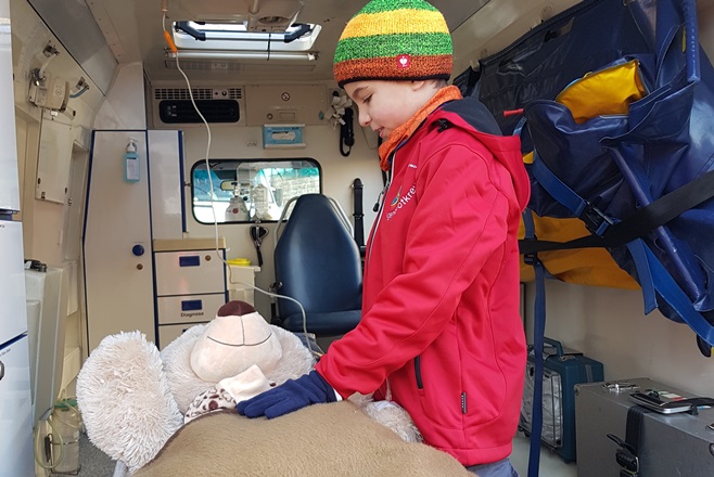 Jugendrotkreuzler verarztet Teddybär im Rettungswagen.